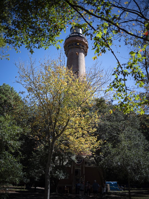 The lighthouse glimpsed through a tree with yellowing autumn leaves.