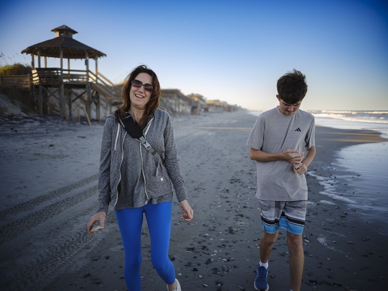 Two people walking down the beach with a wooden gazebo on the dune behind them.